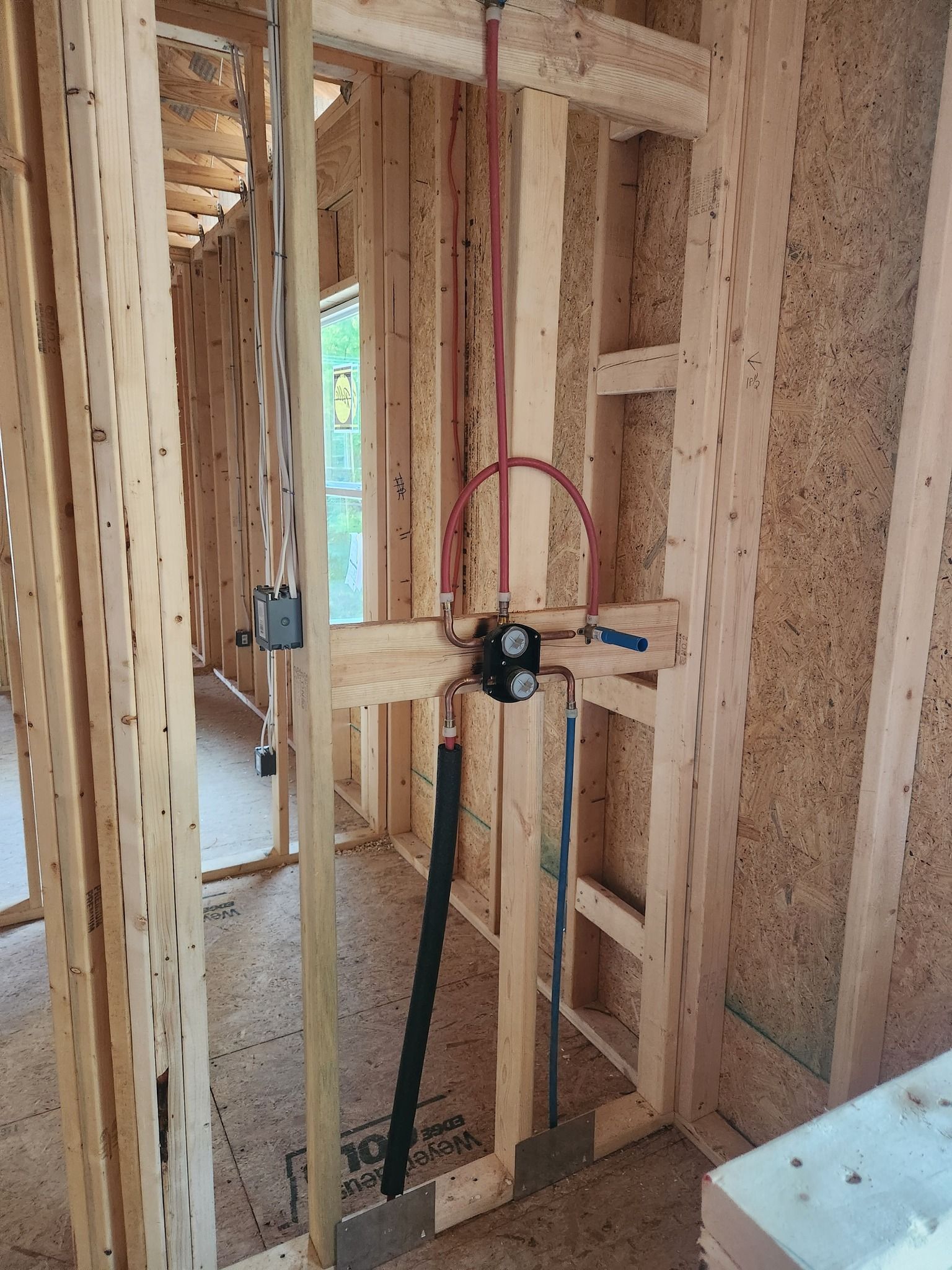 Framed wall with electrical box, wiring, and plumbing pipes in a construction site