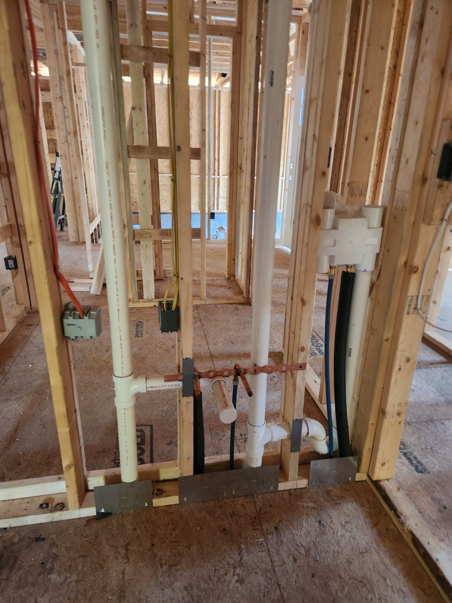 Interior wall framing under construction with exposed studs, wiring, and plumbing pipes.