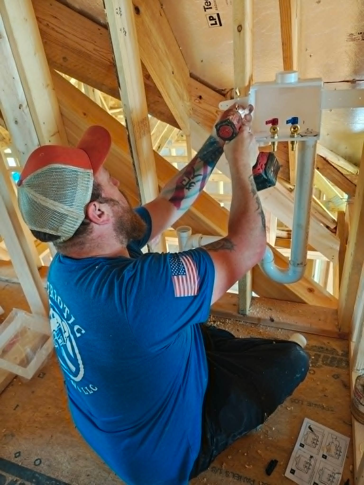 Worker installing pipes in a wooden attic, using tools beside a wall-mounted plumbing unit