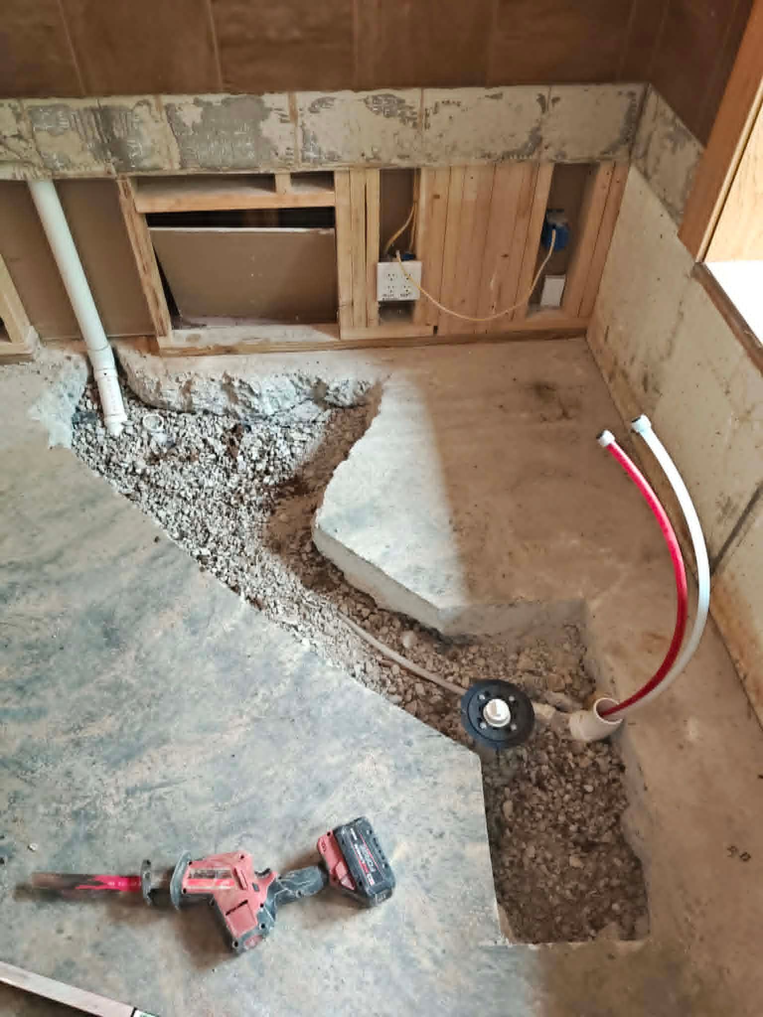 Bathroom under renovation with exposed plumbing, open wall studs, and debris on the floor