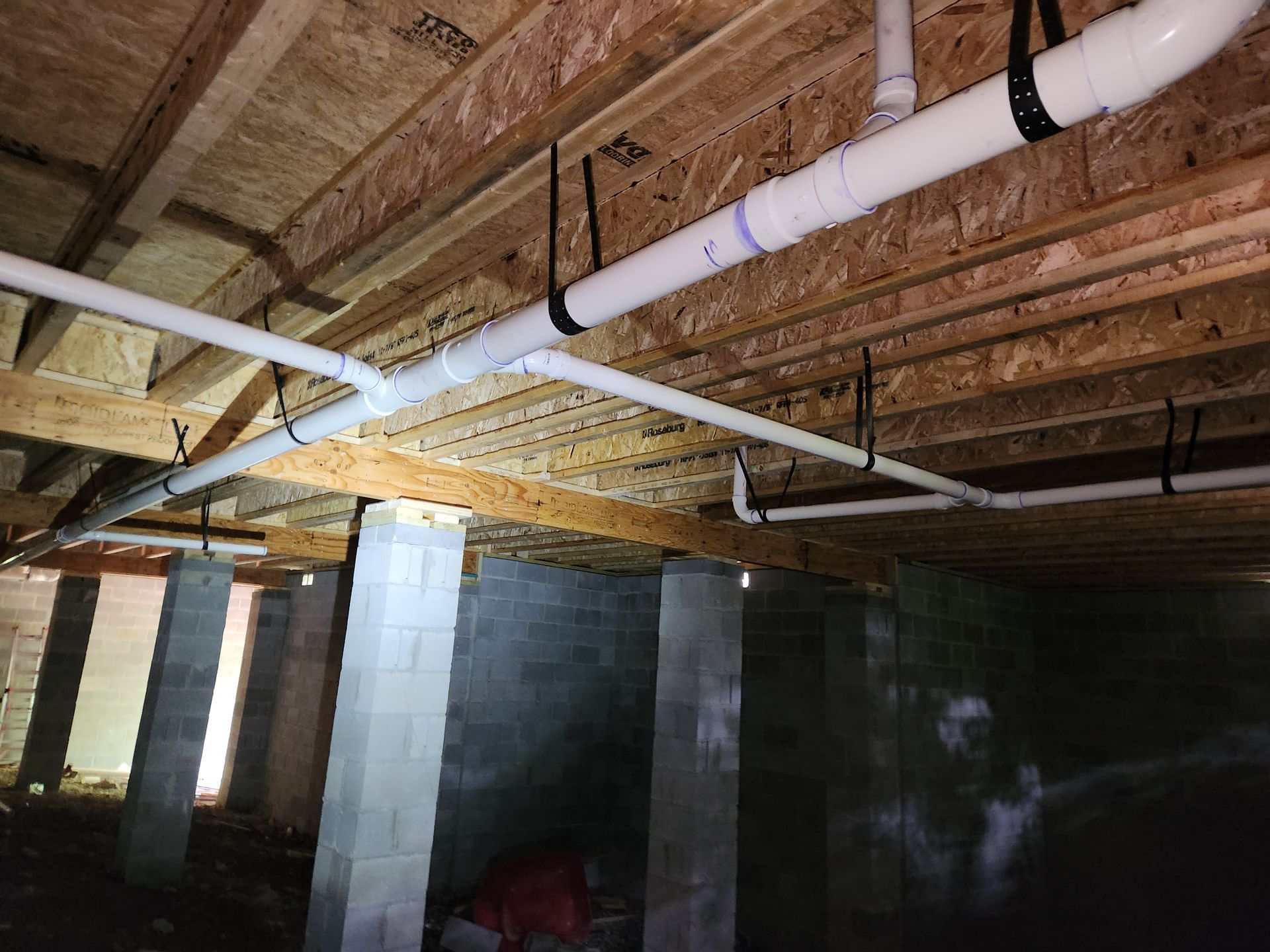 Basement with exposed wood joists, PVC ductwork, and cinder block walls under construction