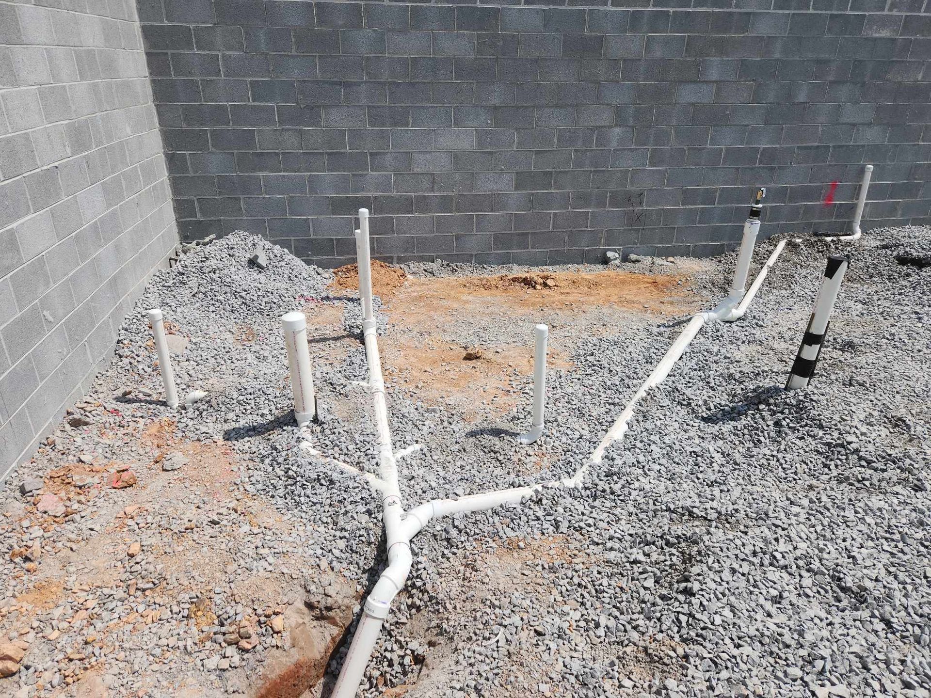 Construction site with gravel, white PVC pipes, and cinder block walls