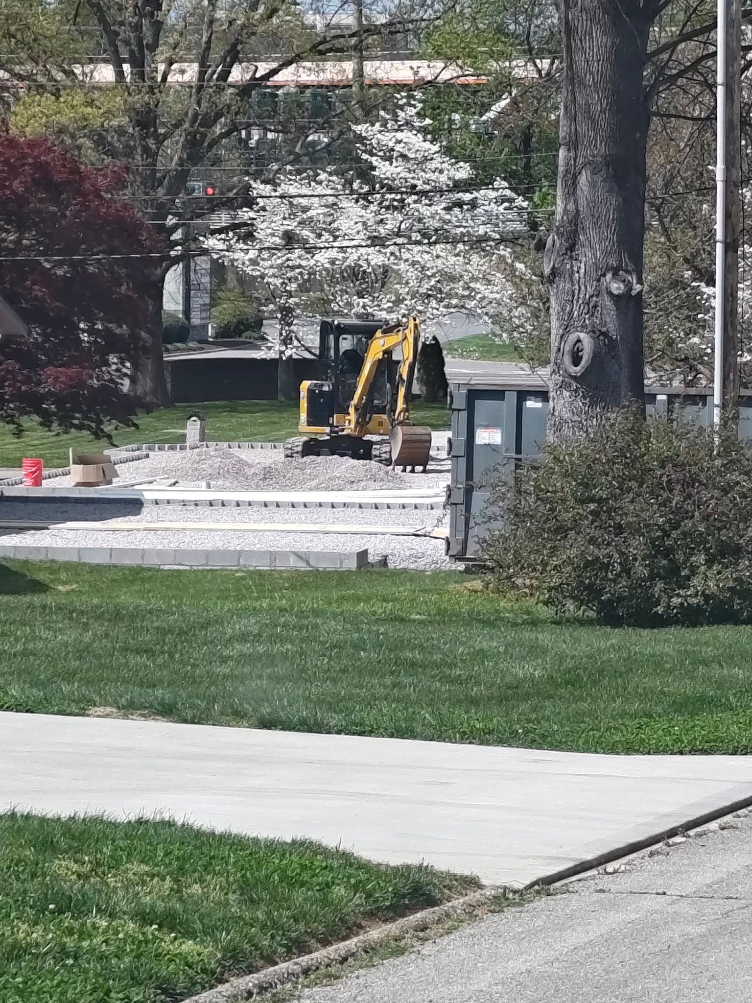 Yellow backhoe in a landscaped park near a walkway and trees
