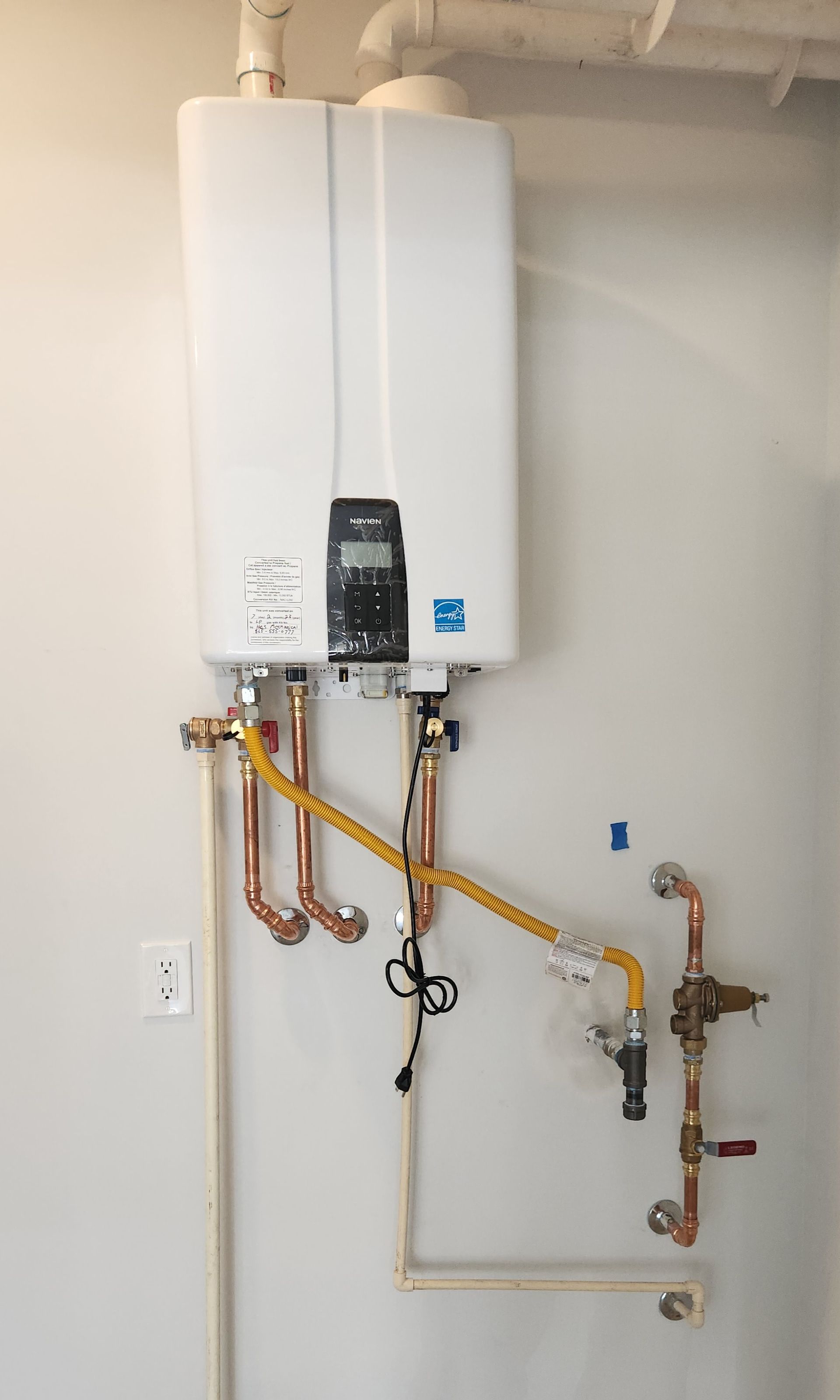 Wall-mounted white tankless water heater with exposed pipes in a utility room.