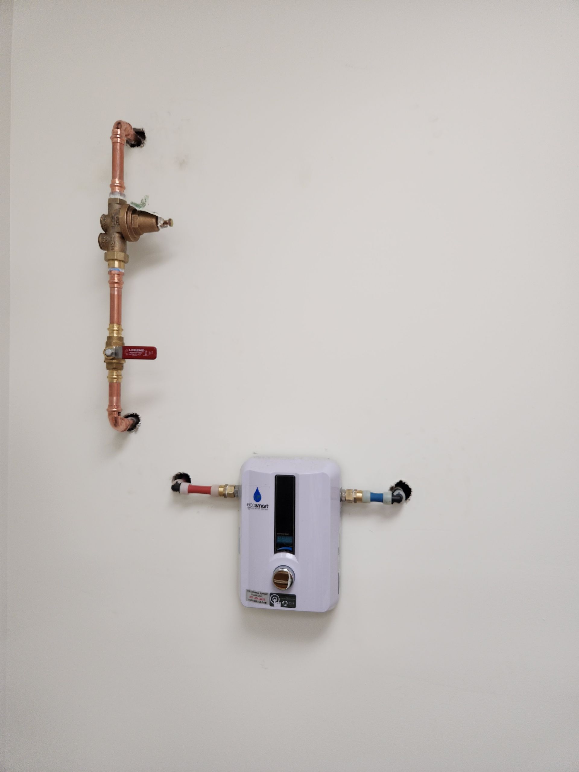 Wall-mounted white water heater with exposed copper pipes and valves on a plain wall.