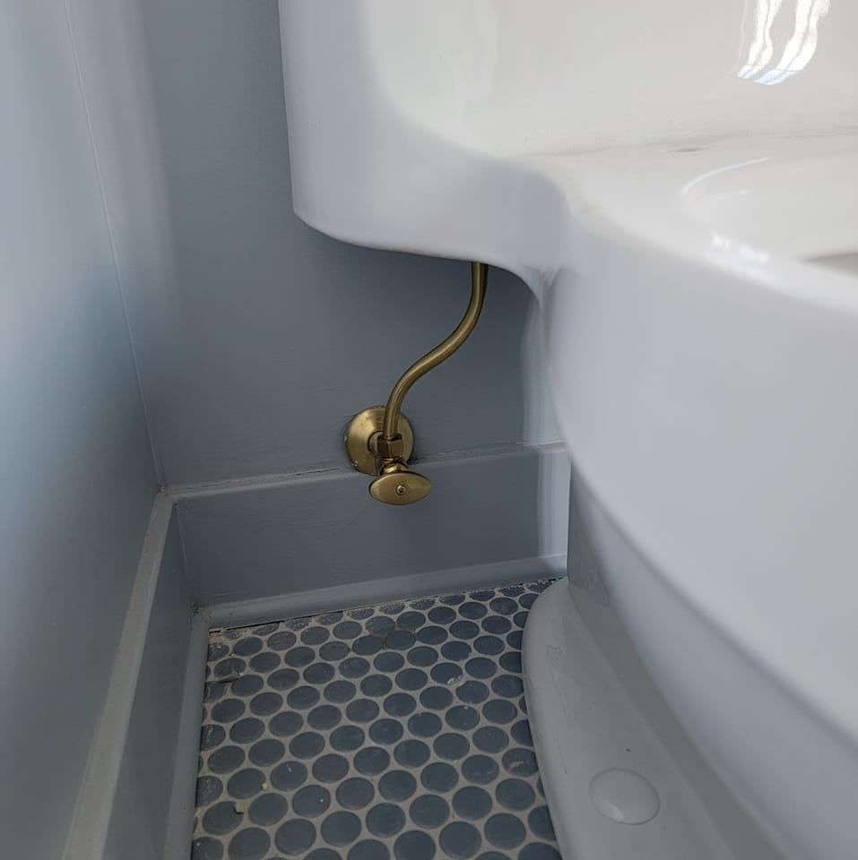 White toilet in a tight bathroom corner with a gold water supply line and blue hex tile floor