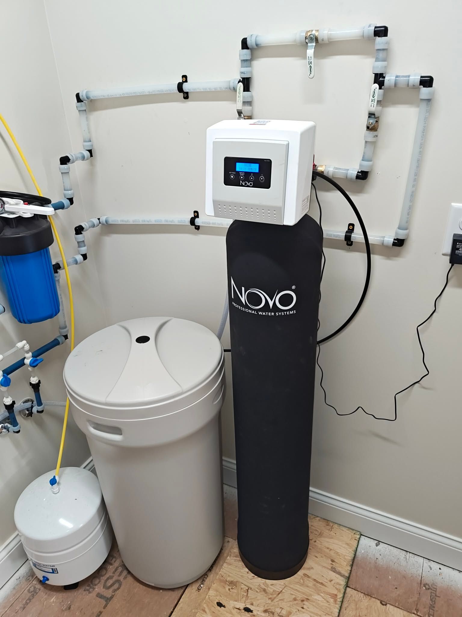 Water treatment system with black tank, control panel, pipes, and blue filter in a utility room