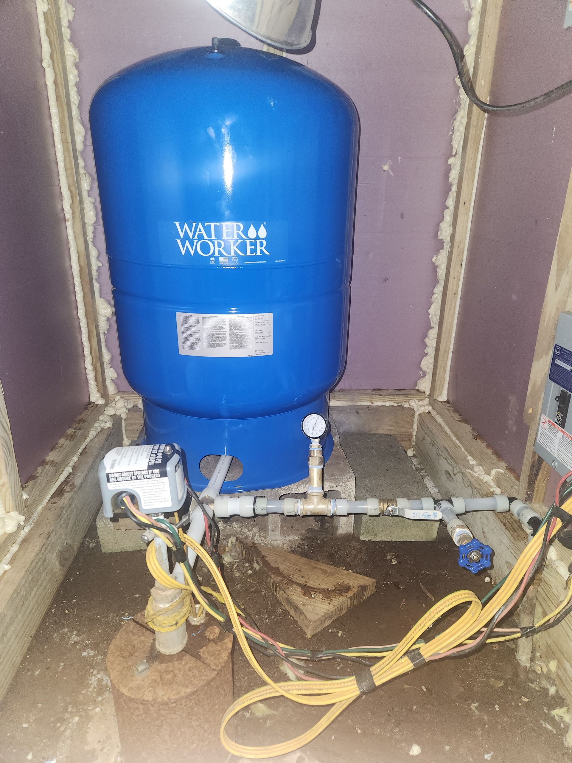 Blue pressure tank and exposed pipes in a utility room with hoses and a pump assembly.