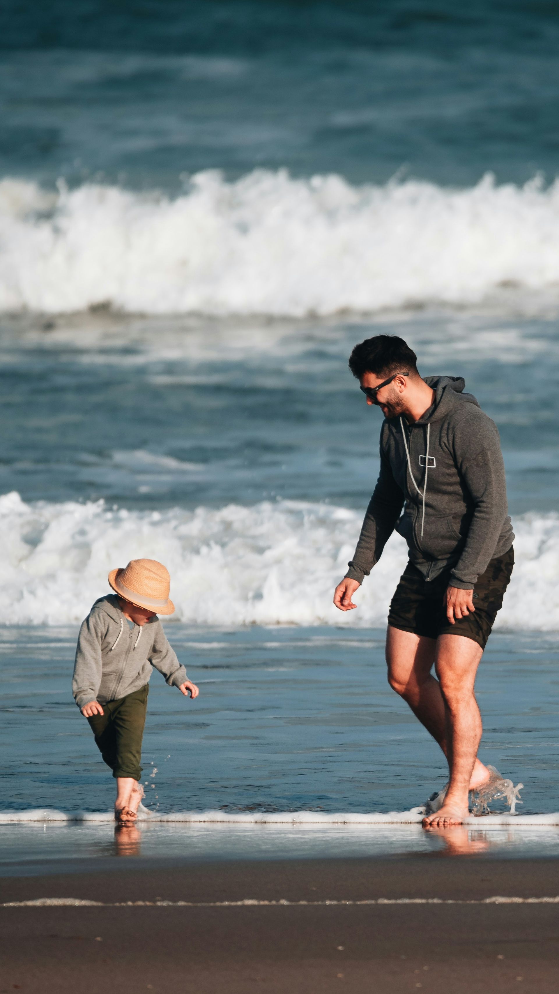 A man and a child are walking on the beach.