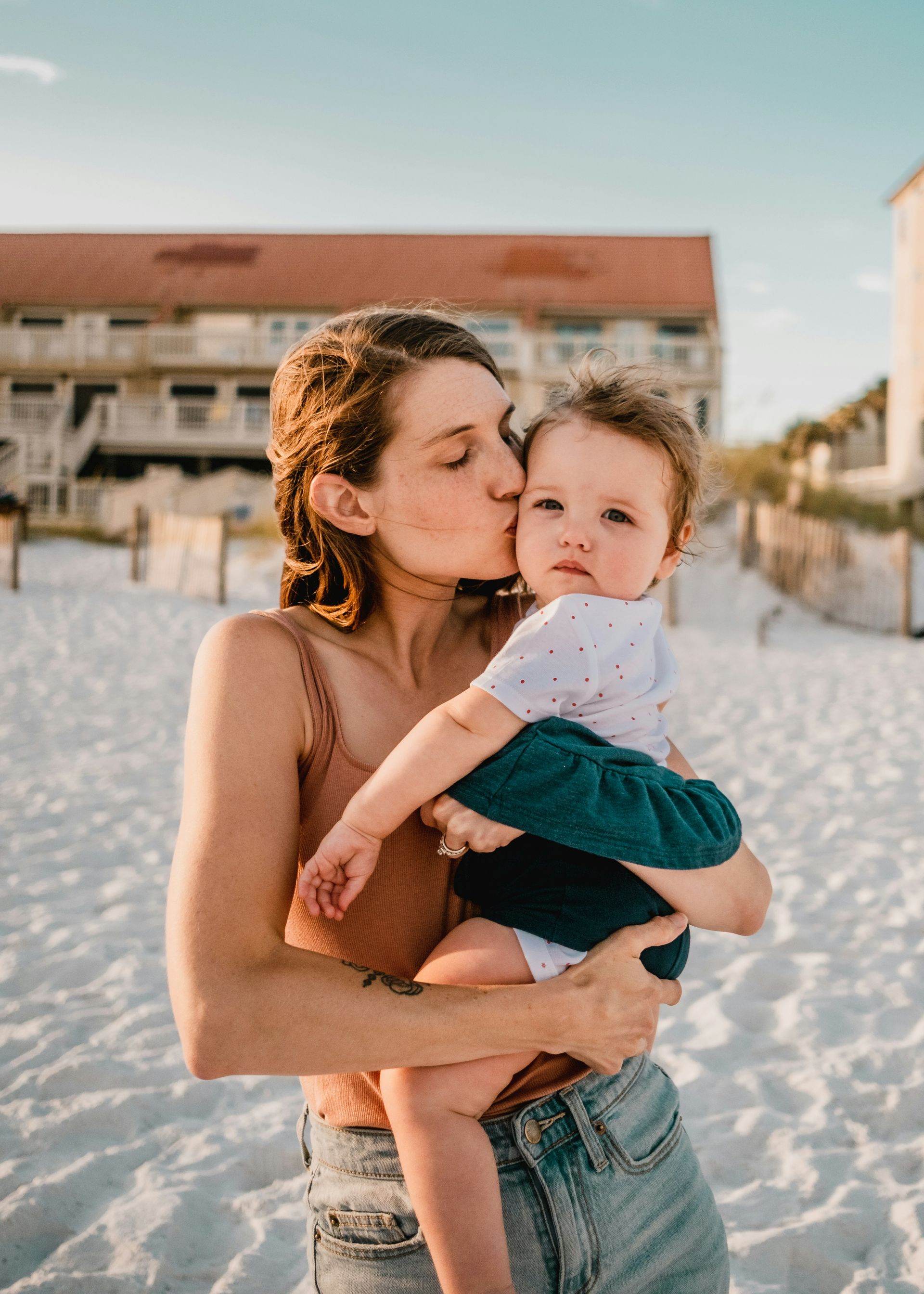 A woman is kissing a baby on the cheek on the beach.