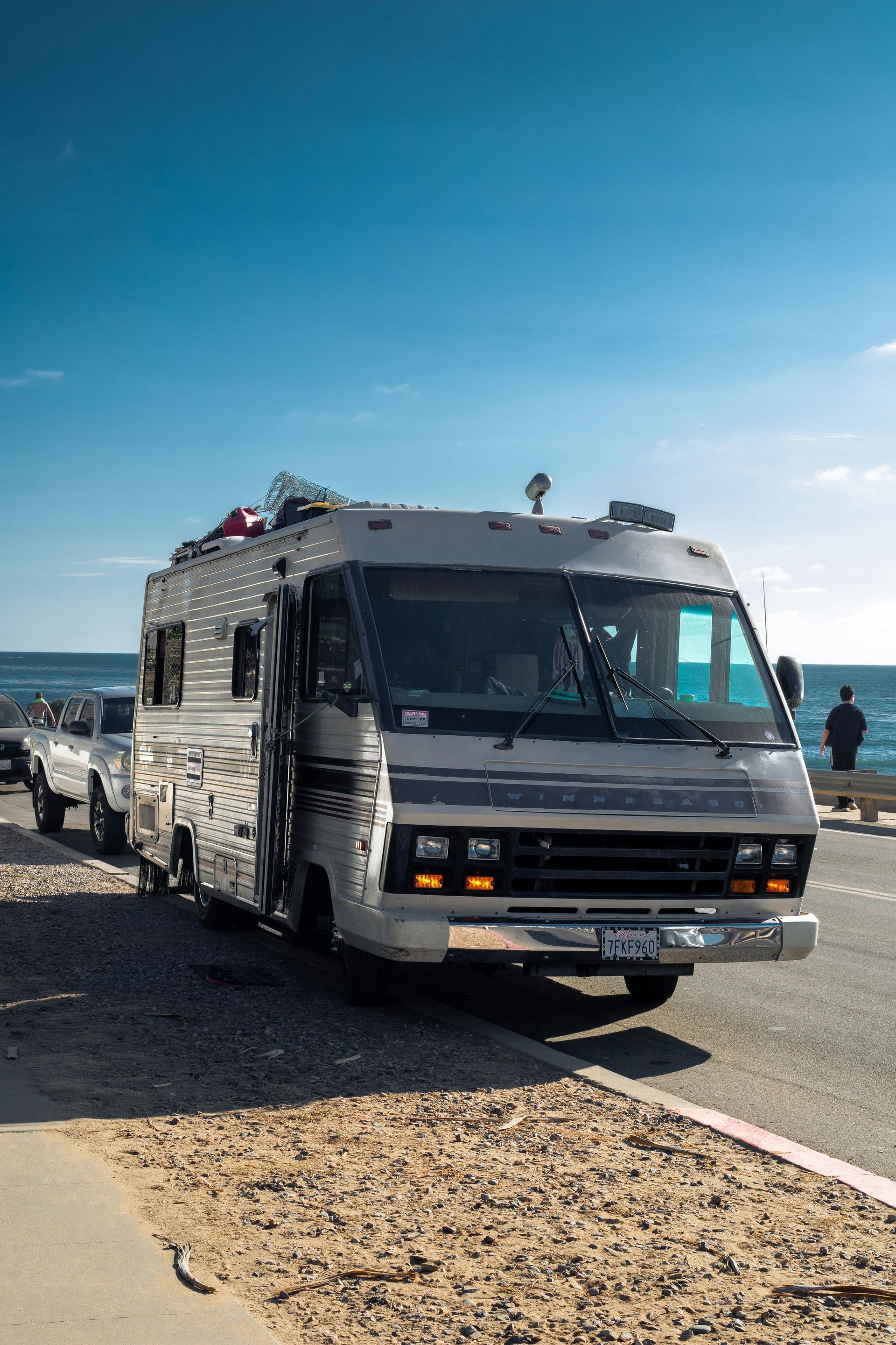 A rv is parked on the side of the road next to the ocean.