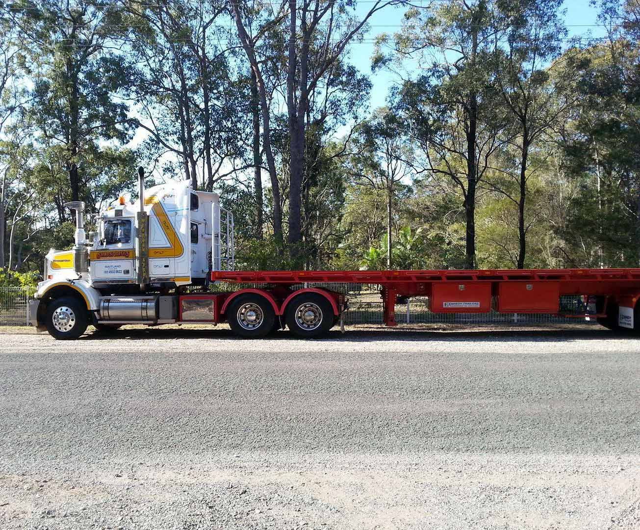 White Kenworth Semi-Truck With A Red Flatbed Trailer