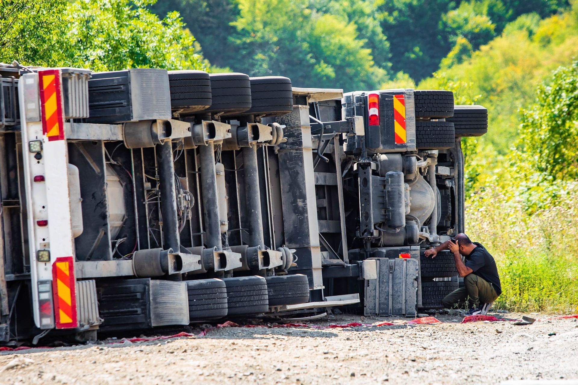 Large cargo truck turned over on the side of a road after an accident. The driver is besides it. Large cargo truck turned over on the side of a road after an accident. The driver is besides it.
