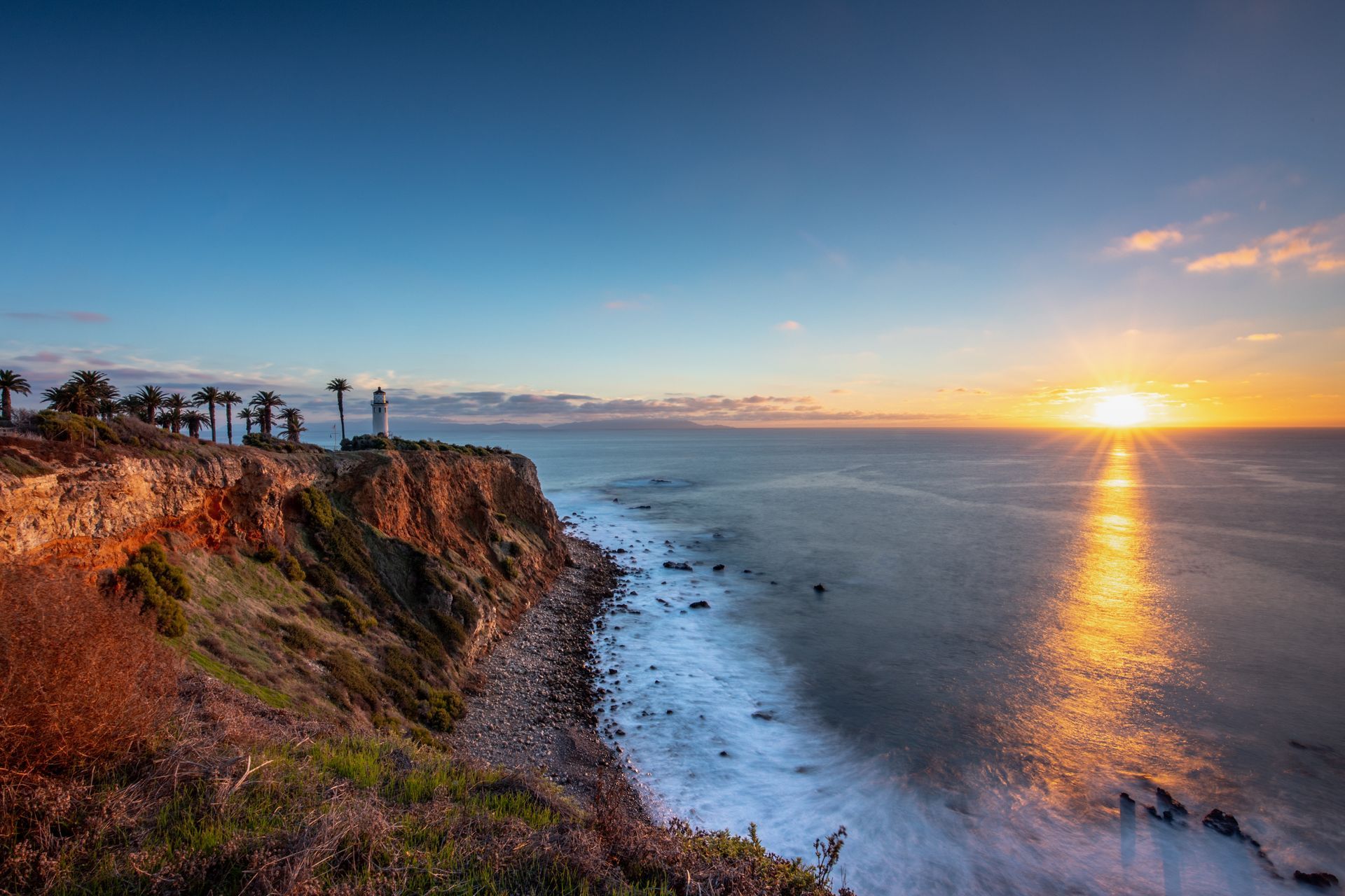 Sunset over a rocky coastline, with ocean waves and golden light reflecting on the water