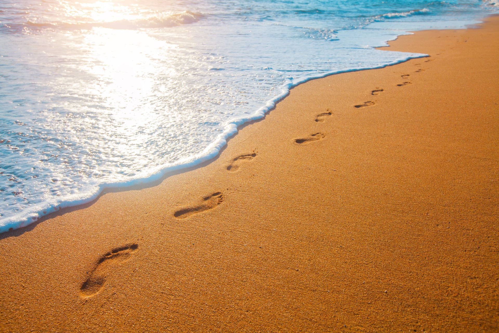 Footprints in golden sand beside a foamy shoreline at sunrise