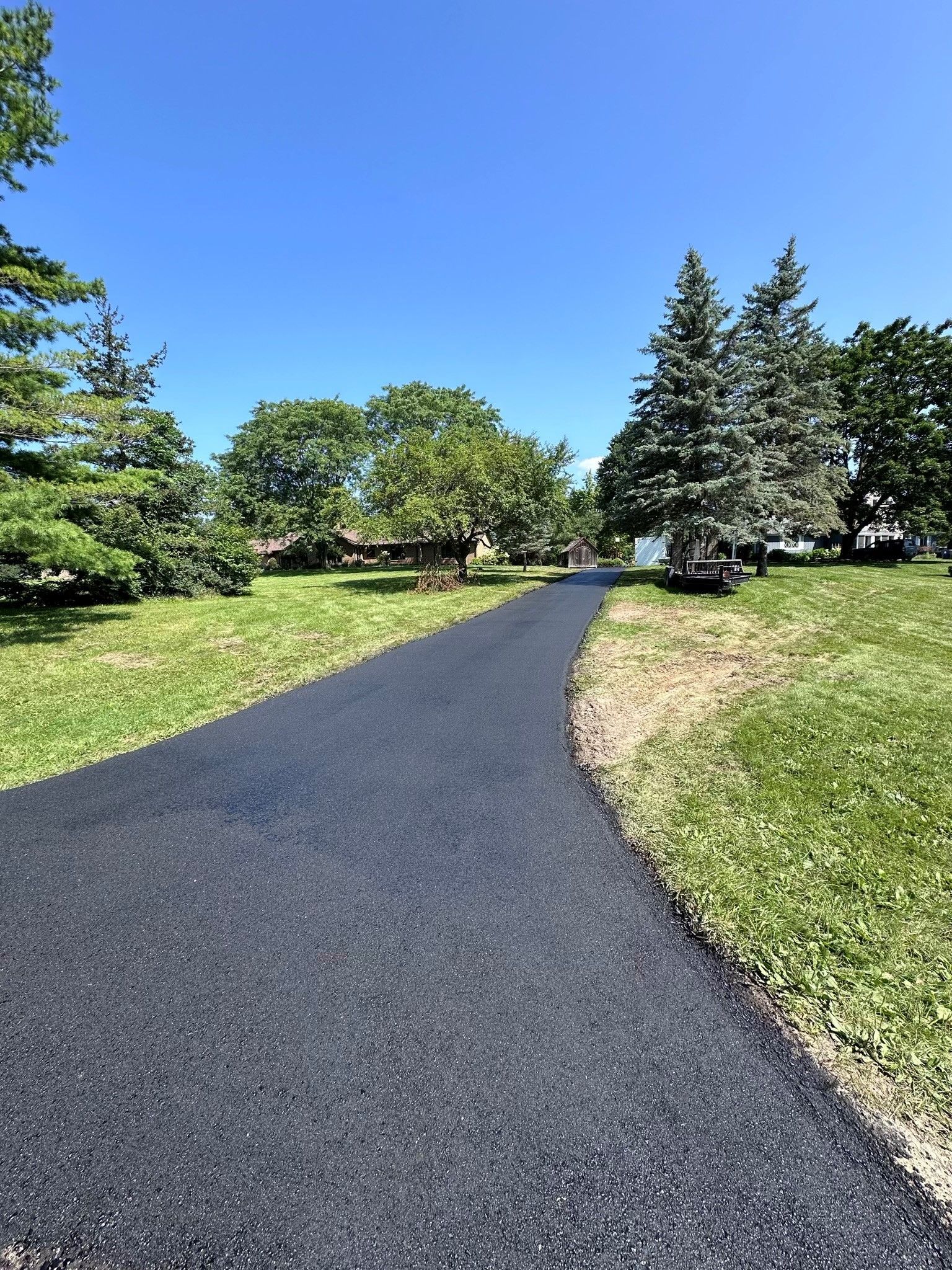 Paved path through a green park under a bright blue sky, with trees and grass lining both sides
