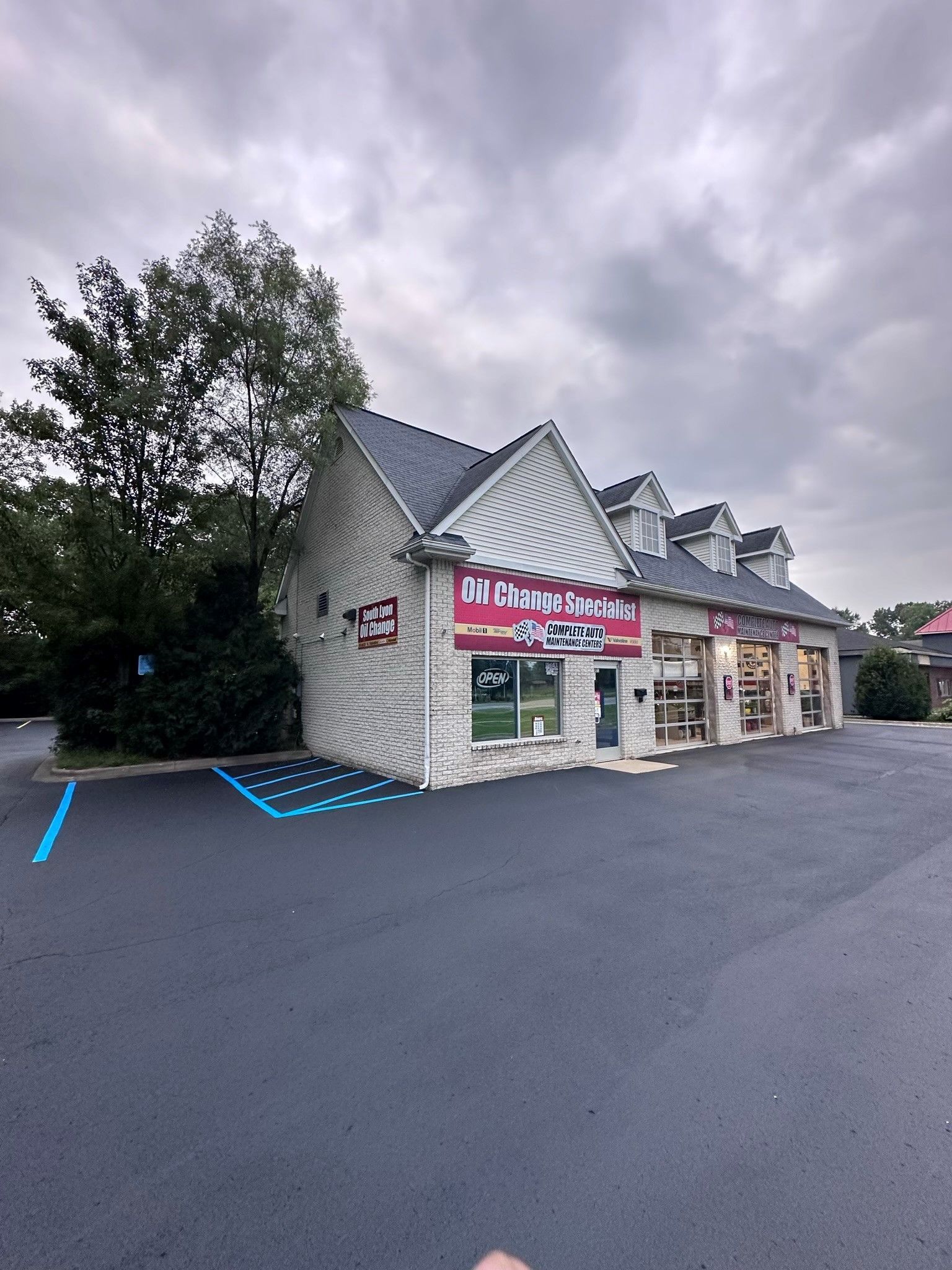 Small roadside shop with red sign and white siding on a cloudy day, viewed from an empty parking lot