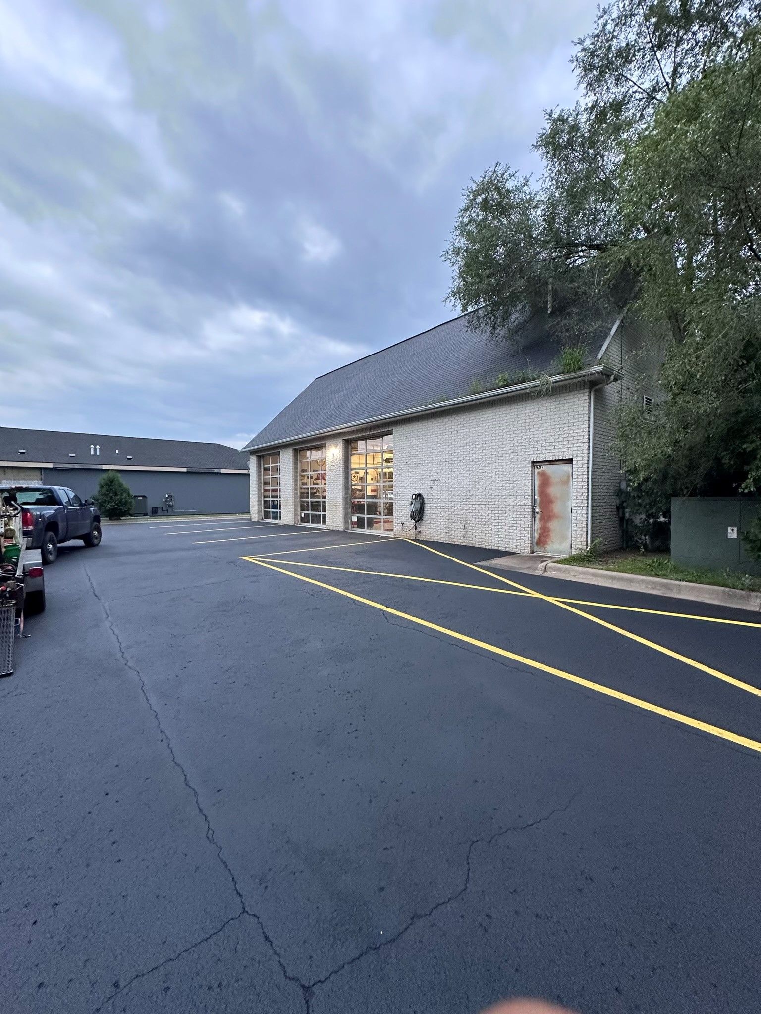 Stone building with lit entrance beside a parking lot under a cloudy sky