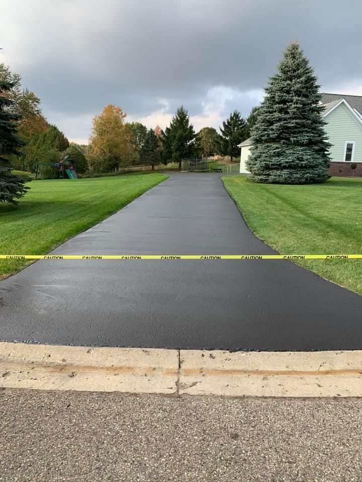 Freshly paved driveway blocked by yellow caution tape in a suburban yard
