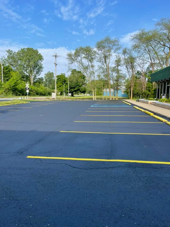 Empty blue parking lot with yellow lines, trees, and a building under a clear sky