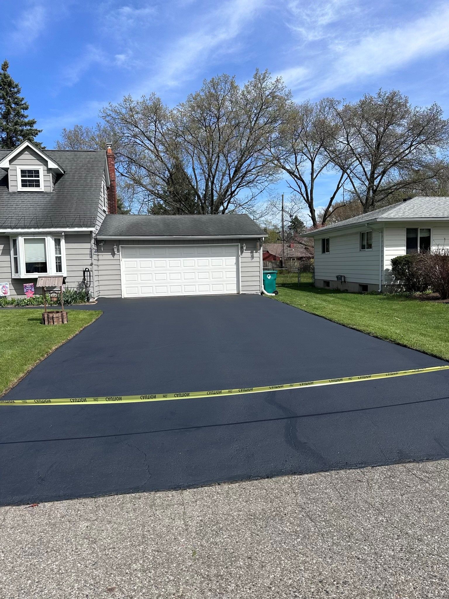 Fresh blacktop driveway leading to a white garage between two houses under a blue sky