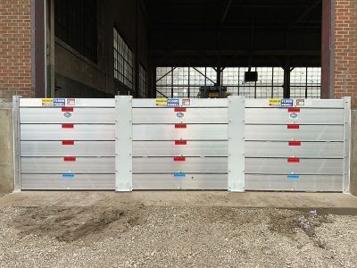 A row of aluminum flood barriers in front of a brick building.