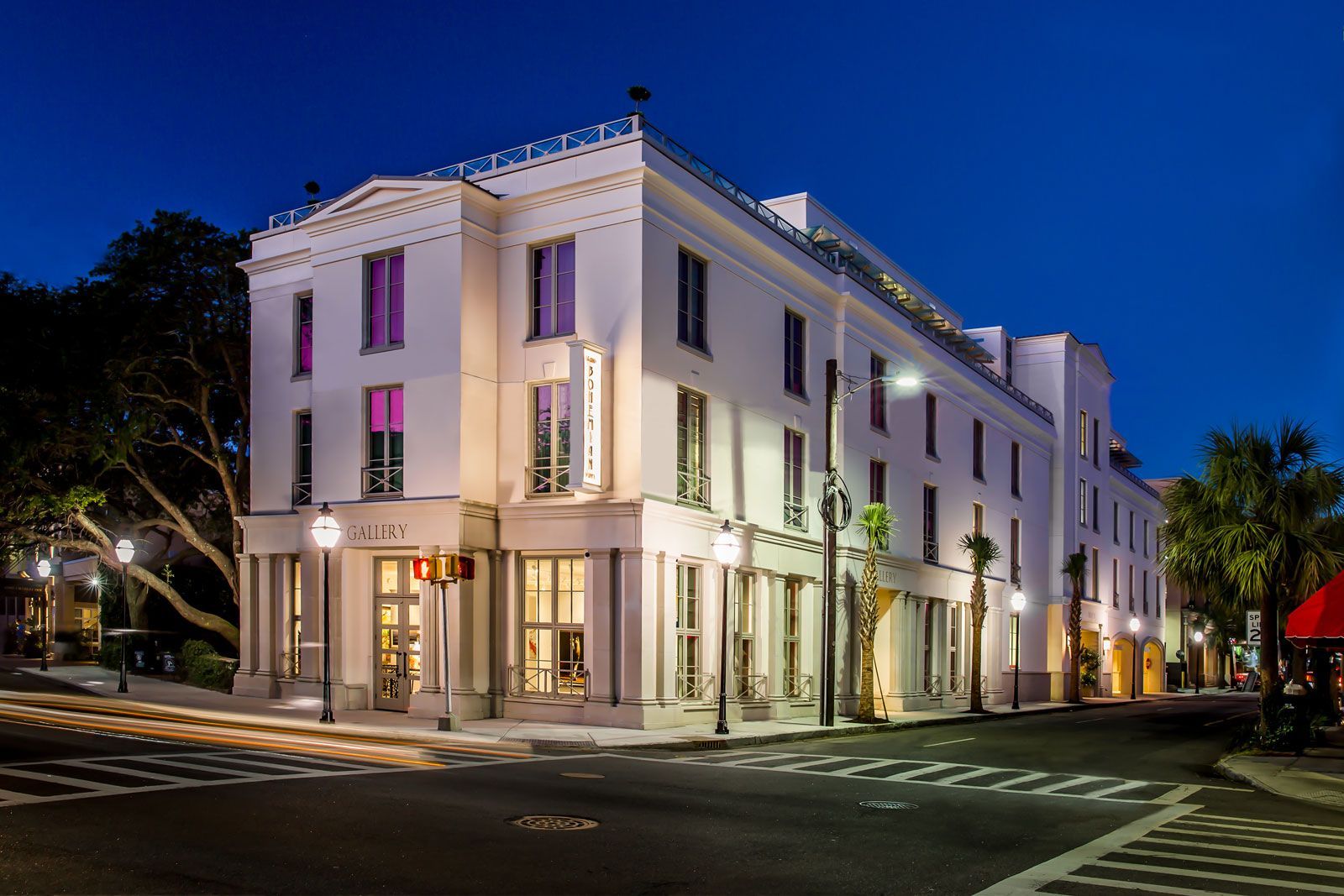 A large white building is sitting on the corner of a street at night.