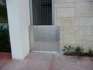 A metal gate is sitting on the side of a building next to a brick wall.