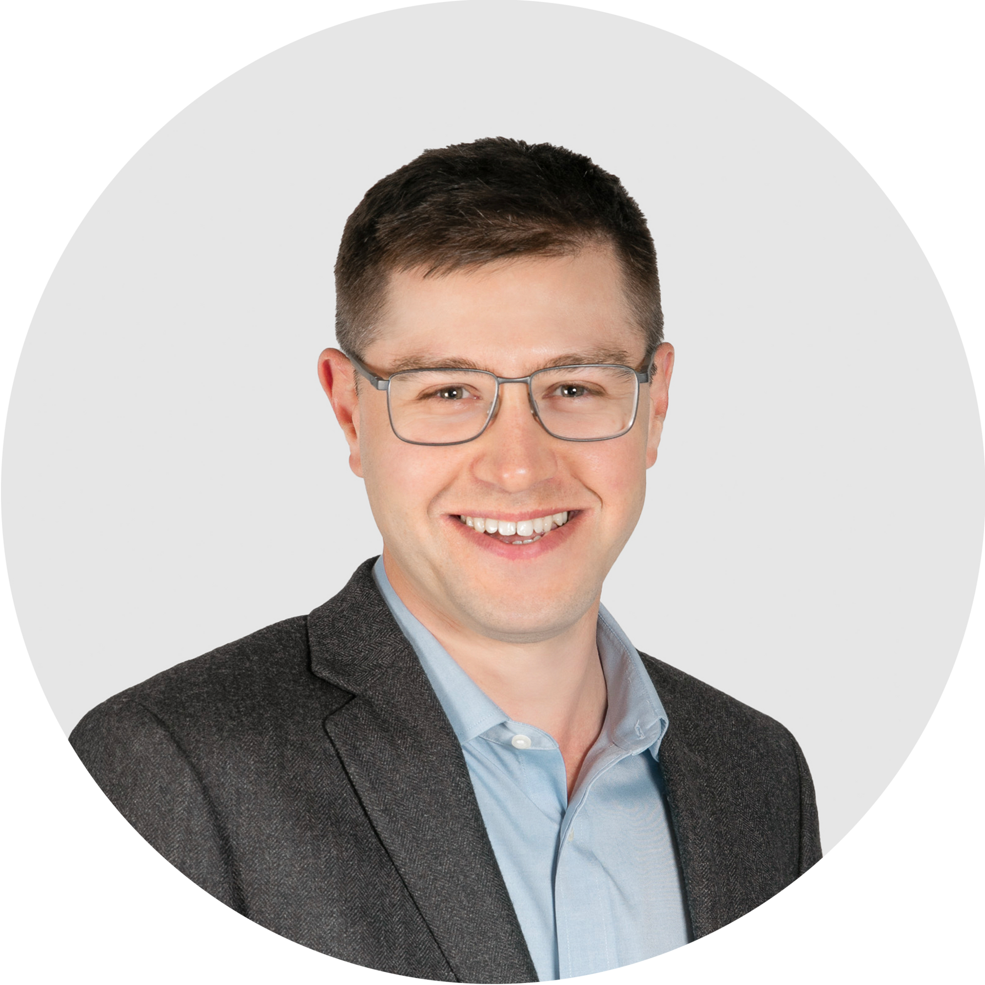 A man wearing glasses and a striped shirt is standing in front of a white background.