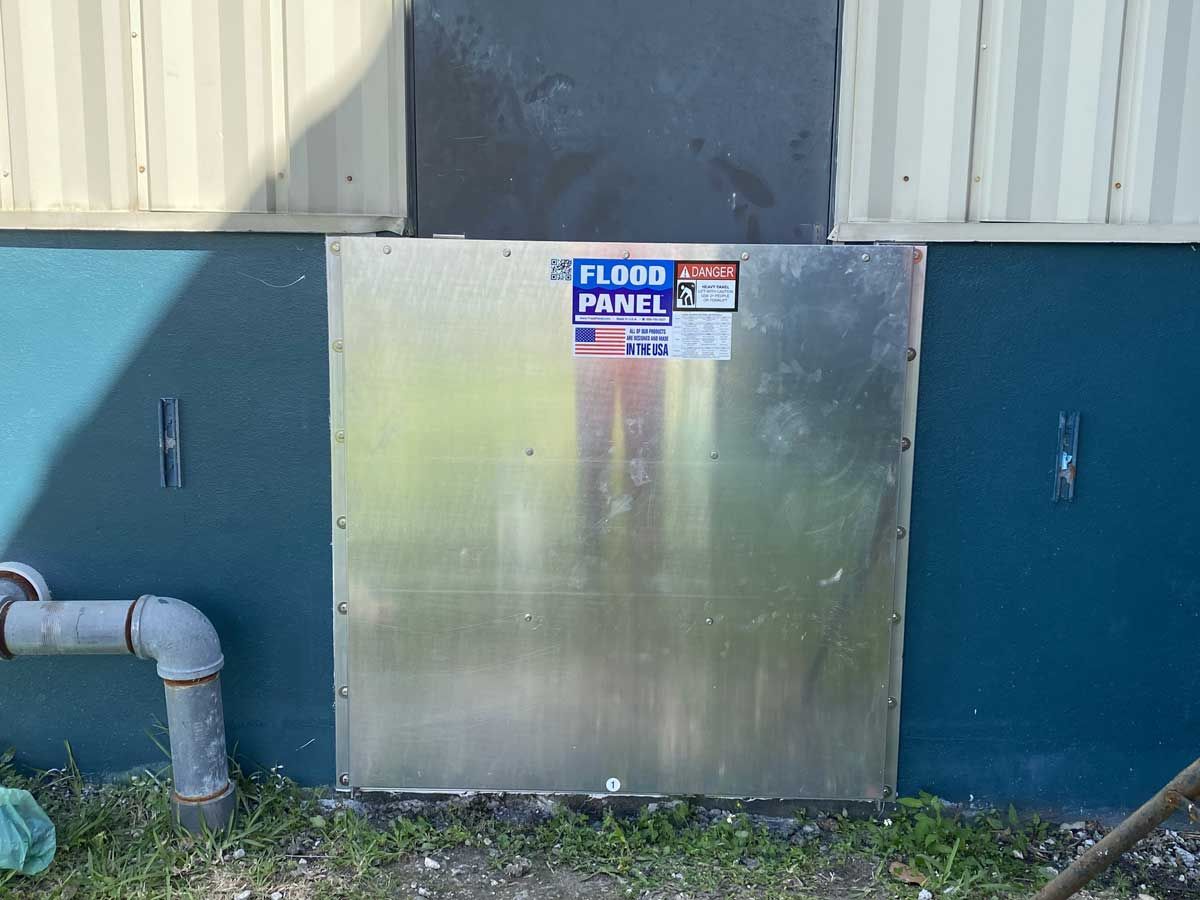A flood panel is sitting on the side of a building next to a pipe.