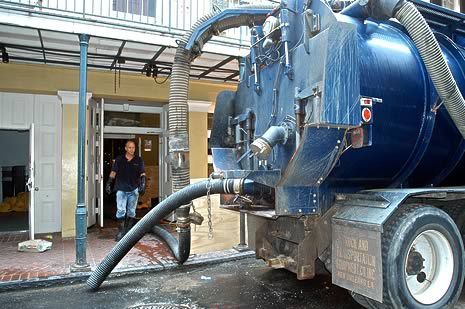 A man is standing in front of a blue vacuum truck.