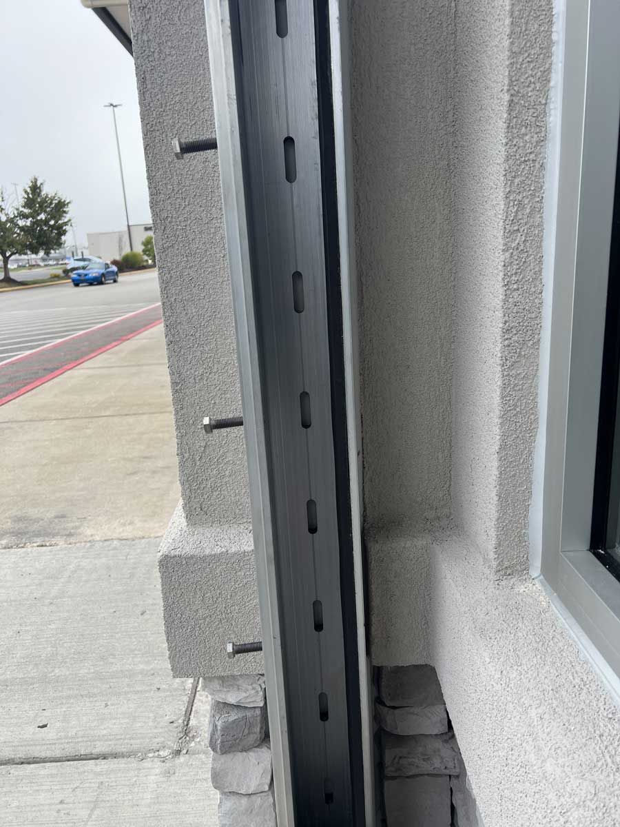 A gray building with a window and a black pole on the side of it.