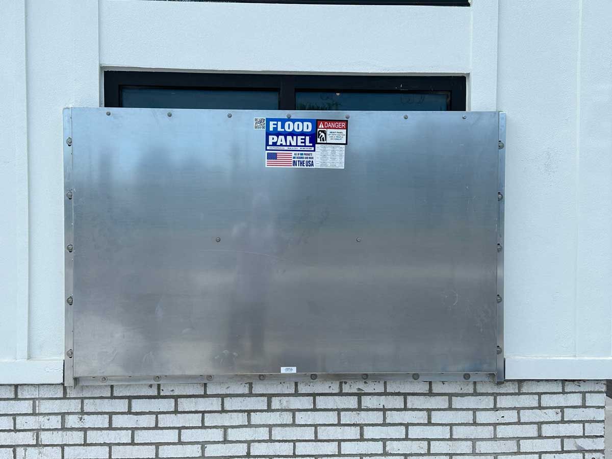 A large metal box is sitting on a brick wall next to a window.
