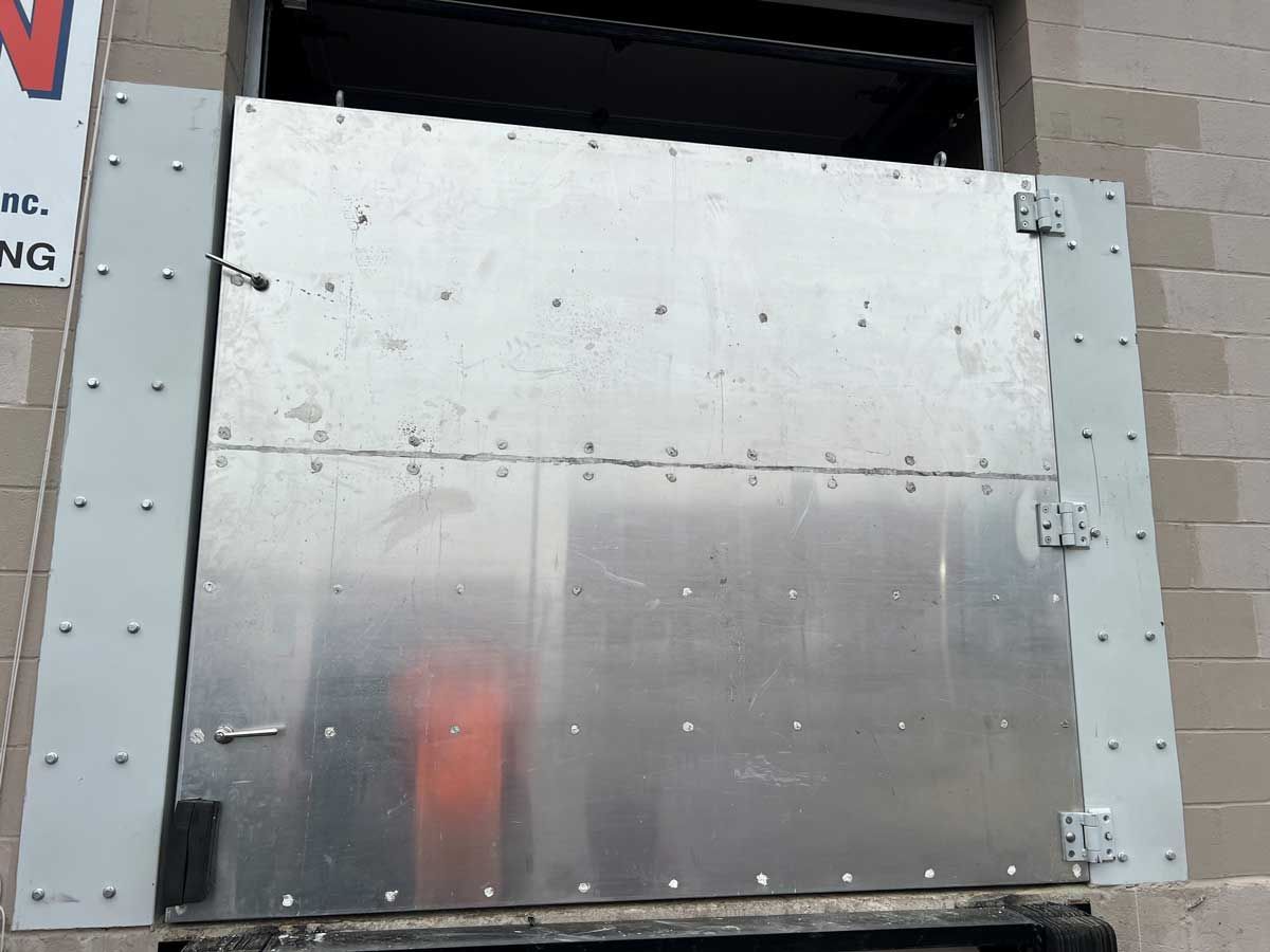 A metal door is sitting on a brick wall next to a sign that says no parking