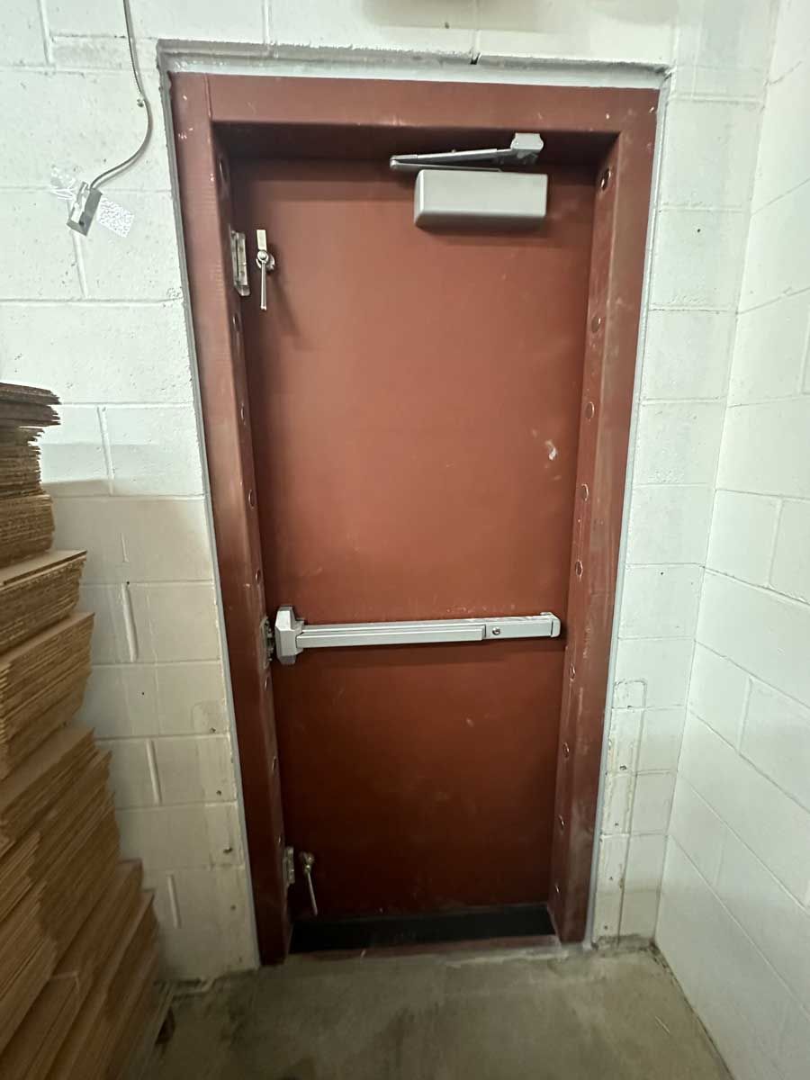 A red door with a white handle is in a room next to a stack of cardboard boxes.