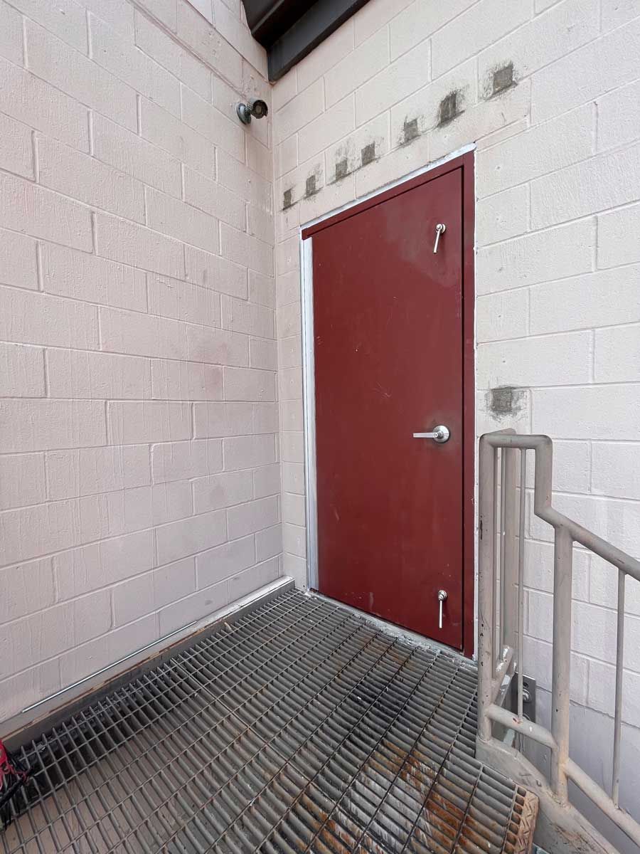 A red door is next to a metal staircase.