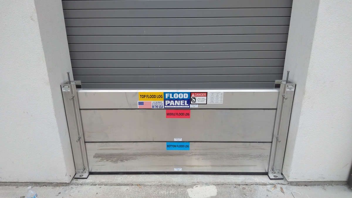 A stainless steel flood barrier is attached to a garage door.
