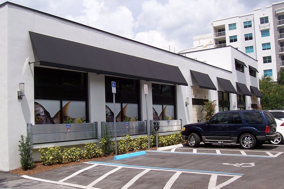 A black suv is parked in front of a white building with black awnings