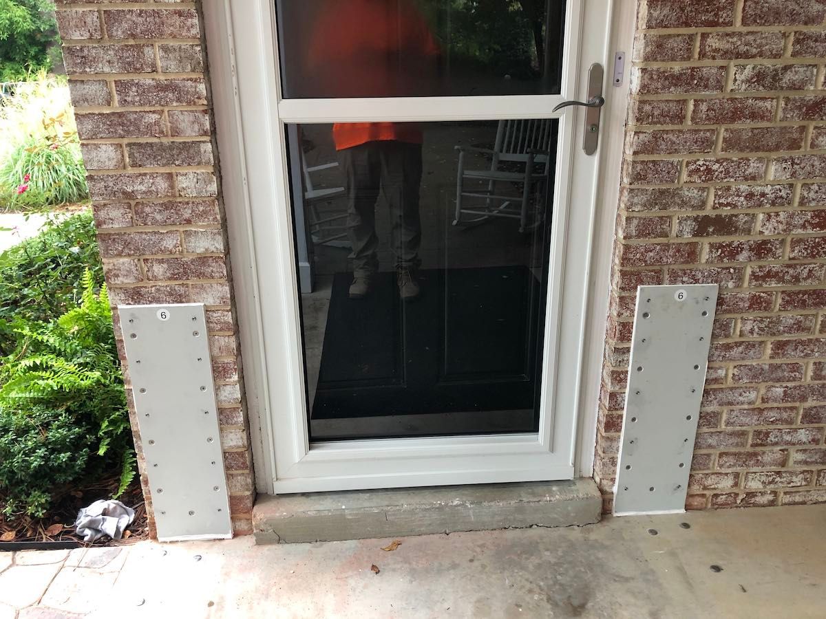 A man is standing in front of a screen door on a brick wall.