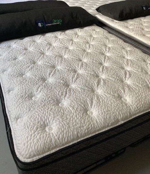 A white mattress with black pillows is sitting on top of a bed.