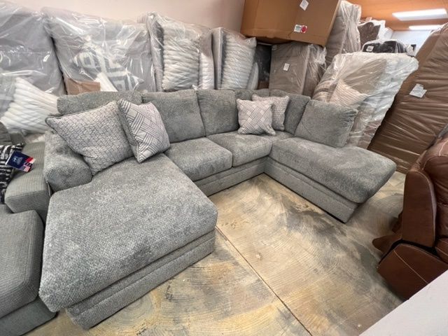 A large sectional couch is sitting in a room surrounded by boxes.