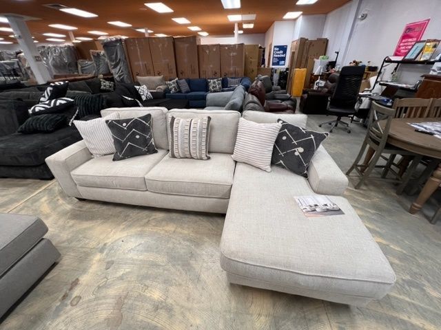 A white sectional couch is in a store surrounded by other furniture