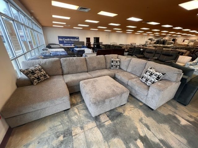 A large sectional couch with an ottoman in a store.