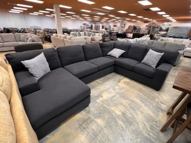 A large sectional couch is sitting in a large room filled with furniture.