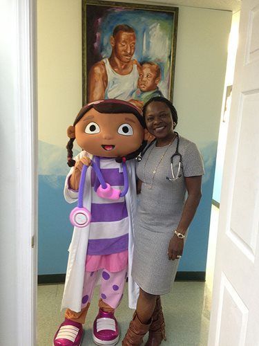 Woman standing with a large character mascot in a hallway, both smiling near a portrait.