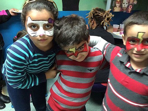 Three children with face paint pose together in striped shirts at a party.