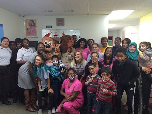 Group photo of people and costumed characters posing indoors in a room with white walls.