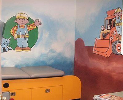Cartoon firefighter mural above a yellow cabinet in a child’s room, with a truck and a penguin on the wall.