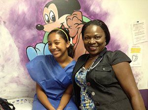 Two smiling women posing in front of a cartoon mural in a bright indoor setting
