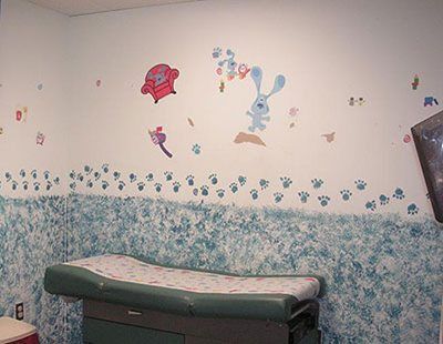 Pediatric exam room with a patterned exam table and whimsical wall decals on a white-and-blue wall